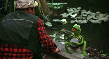 Movie still from “The Muppet Movie” (1979), directed by James Frawley – A man sitting next to a frog holding a guitar; Medium shot, Over the shoulder angle