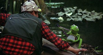 Movie still from “The Muppet Movie” (1979), directed by James Frawley – A man holding a guitar next to a green frog; Medium shot, Over the shoulder angle
