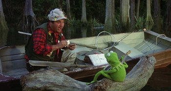 Movie still from “The Muppet Movie” (1979), directed by James Frawley – A man sitting in a boat next to kermit the frog; Medium shot, Over the shoulder angle