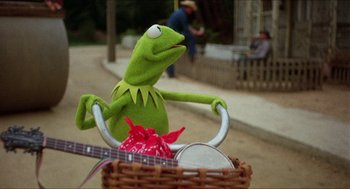 Movie still from “The Muppet Movie” (1979), directed by James Frawley – A green stuffed animal sitting on top of a bicycle; Medium shot, Low angle