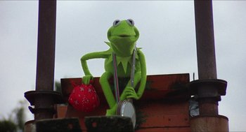 Movie still from “The Muppet Movie” (1979), directed by James Frawley – A green stuffed animal holding a red bag; Medium shot, Low angle