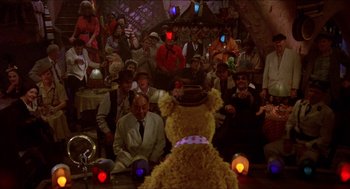Movie still from “The Muppet Movie” (1979), directed by James Frawley – A crowd of people sitting around a teddy bear; Wide shot, High angle