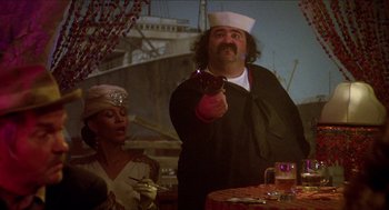 Movie still from “The Muppet Movie” (1979), directed by James Frawley – A man holding a wine glass while standing next to a woman; Medium shot, Over the shoulder angle