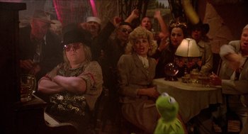 Movie still from “The Muppet Movie” (1979), directed by James Frawley – A group of people sitting in a room with kermit the frog in the background; Medium shot, Over the shoulder angle