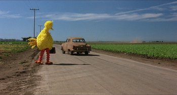 Movie still from “The Muppet Movie” (1979), directed by James Frawley – A big bird costume stands in front of an old car on the side of the road; Wide shot, Low angle