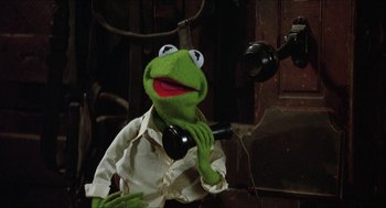 Movie still from “The Muppet Movie” (1979), directed by James Frawley – A kermit the frog wearing a white shirt holding a phone; Close Up shot, High angle