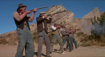 Movie still from “The Muppet Movie” (1979), directed by James Frawley – A group of men standing next to each other holding guns; Wide shot, Low angle