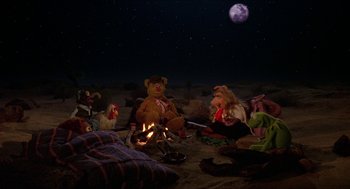 Movie still from “The Muppet Movie” (1979), directed by James Frawley – A group of people sitting next to a fire pit at night; Wide shot, High angle