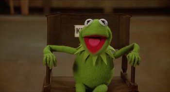 Movie still from “The Muppet Movie” (1979), directed by James Frawley – Kermit the frog sitting in a chair with his arms spread out; Medium shot, Low angle