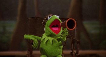 Movie still from “The Muppet Movie” (1979), directed by James Frawley – A kermit the frog puppet holding a microphone up to his mouth; Close Up shot, Low angle