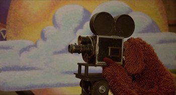 Movie still from “The Muppet Movie” (1979), directed by James Frawley – A teddy bear is holding a movie camera on top of a dolly; Extreme Close Up shot, Low angle