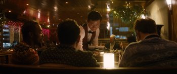 Movie still from “The Night Before” (2015), directed by Jonathan Levine – A man standing at a table in front of two other men; Medium shot, Over the shoulder angle