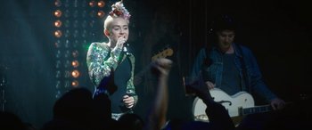 Movie still from “The Night Before” (2015), directed by Jonathan Levine – A woman in a green dress singing into a microphone; Medium shot, Over the shoulder angle