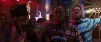 Movie still from “The Night Before” (2015), directed by Jonathan Levine – A man wearing a christmas sweater is holding something up; Medium shot, Over the shoulder angle
