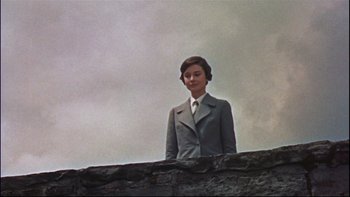 Movie still from “The Nun's Story” (1959), directed by Fred Zinnemann – A woman in a suit standing on top of a stone wall; Medium shot, Low angle