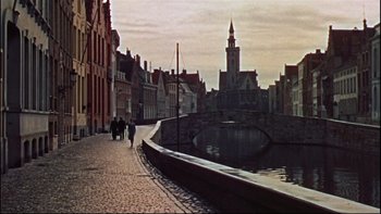 Movie still from “The Nun's Story” (1959), directed by Fred Zinnemann – People walking down a sidewalk near a river; Extreme Wide shot, High angle