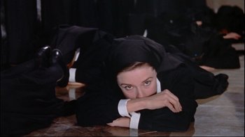 Movie still from “The Nun's Story” (1959), directed by Fred Zinnemann – A woman laying on the ground wearing a black suit; Medium shot, Overhead angle