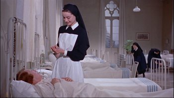 Movie still from “The Nun's Story” (1959), directed by Fred Zinnemann – A nun standing next to a bed in a room; Medium shot, Overhead angle
