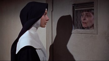 Movie still from “The Nun's Story” (1959), directed by Fred Zinnemann – A nun looking at a woman through a window; Medium shot, Low angle