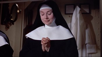 Movie still from “The Nun's Story” (1959), directed by Fred Zinnemann – A woman in a nun's habit praying with her hands together; Close Up shot, Low angle