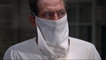 Movie still from “The Nun's Story” (1959), directed by Fred Zinnemann – A man wearing a face mask and looking at the camera; Close Up shot, Low angle