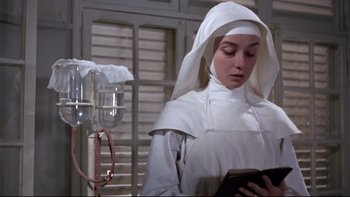 Movie still from “The Nun's Story” (1959), directed by Fred Zinnemann – A woman in a nun's outfit standing next to a hospital bed; Medium shot, Low angle