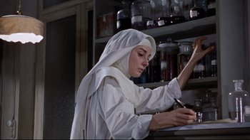 Movie still from “The Nun's Story” (1959), directed by Fred Zinnemann – A nun writing on a piece of paper in front of a counter; Medium shot, Low angle