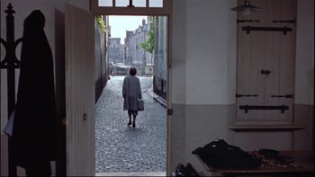 Movie still from “The Nun's Story” (1959), directed by Fred Zinnemann – An older woman walking down a street with a suitcase; Extreme Wide shot, Over the shoulder angle