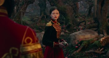 Movie still from “The Nutcracker and the Four Realms” (2018), directed by Joe Johnston – A woman in a military uniform standing in front of a forest; Medium shot, Over the shoulder angle