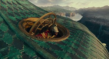 Movie still from “The Nutcracker and the Four Realms” (2018), directed by Joe Johnston – A man wearing a helmet is sitting in a basket on the roof of a building; Wide shot, Overhead angle