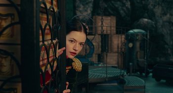 Movie still from “The Nutcracker and the Four Realms” (2018), directed by Joe Johnston – A young woman holding a flower behind a metal fence; Medium shot, Over the shoulder angle