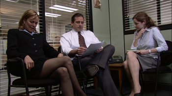 Movie still from “The Office” (2005), created by Ricky Gervais – A man sitting on a chair reading a paper; Wide shot, High angle