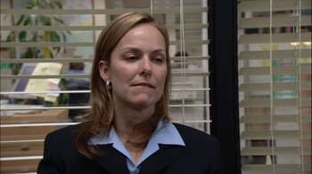 Movie still from “The Office” (2005), created by Ricky Gervais – A woman in a black suit and a blue shirt; Close Up shot, Over the shoulder angle