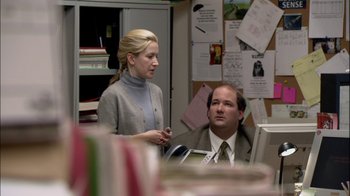 Movie still from “The Office” (2005), created by Ricky Gervais – A woman standing next to a man in an office setting; Medium shot, Over the shoulder angle
