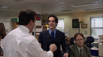 Movie still from “The Office” (2005), created by Ricky Gervais – Two men in suits shaking hands in an office setting; Medium shot, Over the shoulder angle