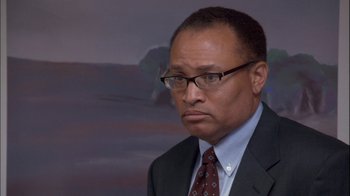 Movie still from “The Office” (2005), created by Ricky Gervais – A man in a suit and tie with glasses; Close Up shot, Over the shoulder angle