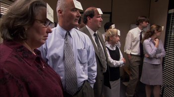 Movie still from “The Office” (2005), created by Ricky Gervais – A group of people standing next to each other with notes stuck on their heads; Medium shot, High angle