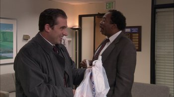 Movie still from “The Office” (2005), created by Ricky Gervais – Two men in business suits are exchanging gifts; Medium shot, Over the shoulder angle