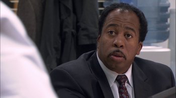 Movie still from “The Office” (2005), created by Ricky Gervais – A man in a suit and tie looking at the camera; Close Up shot, Over the shoulder angle