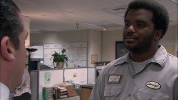 Movie still from “The Office” (2005), created by Ricky Gervais – A man standing in an office wearing a uniform; Medium shot, Over the shoulder angle