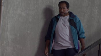 Movie still from “The Office” (2005), created by Ricky Gervais – A man standing in front of a gray wall; Medium shot, High angle