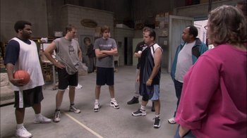 Movie still from “The Office” (2005), created by Ricky Gervais – A group of men standing around in a building; Wide shot, High angle
