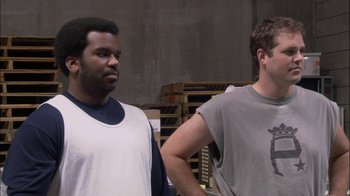 Movie still from “The Office” (2005), created by Ricky Gervais – Two men standing next to each other in front of a wall; Medium shot, Over the shoulder angle
