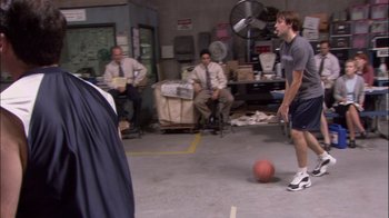 Movie still from “The Office” (2005), created by Ricky Gervais – A group of men playing a game of basketball in a warehouse; Wide shot, Over the shoulder angle