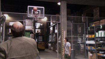 Movie still from “The Office” (2005), created by Ricky Gervais – A man is playing basketball in a warehouse; Extreme Wide shot, High angle