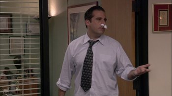 Movie still from “The Office” (2005), created by Ricky Gervais – A man in a dress shirt and a tie with a piece of paper in his mouth; Medium shot, High angle