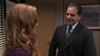 Movie still from “The Office” (2005), created by Ricky Gervais – A man in a suit and tie talking to a woman in a purple dress; Medium shot, Over the shoulder angle