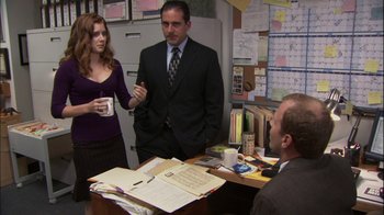 Movie still from “The Office” (2005), created by Ricky Gervais – A group of people standing around a table; Medium shot, Over the shoulder angle