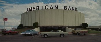 Movie still from “The Old Man & the Gun” (2018), directed by David Lowery – An american bank building with a car parked in front of it; Extreme Wide shot, Low angle