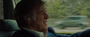 Movie still from “The Old Man & the Gun” (2018), directed by David Lowery – An older man wearing a blue suit and white headphones; Close Up shot, Over the shoulder angle